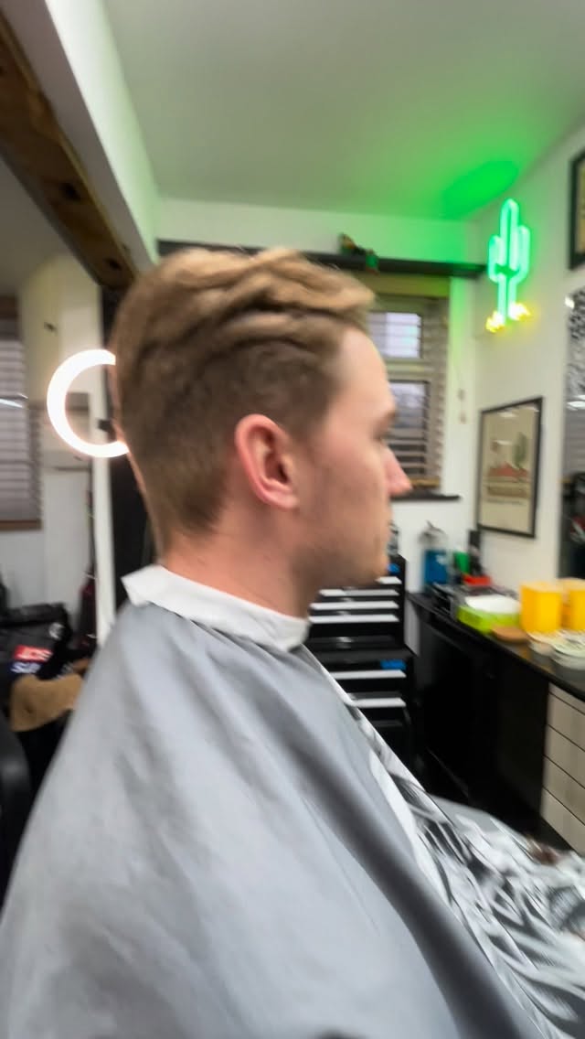 A textured cut with a taper, seen from the side, under the shop’s green neon